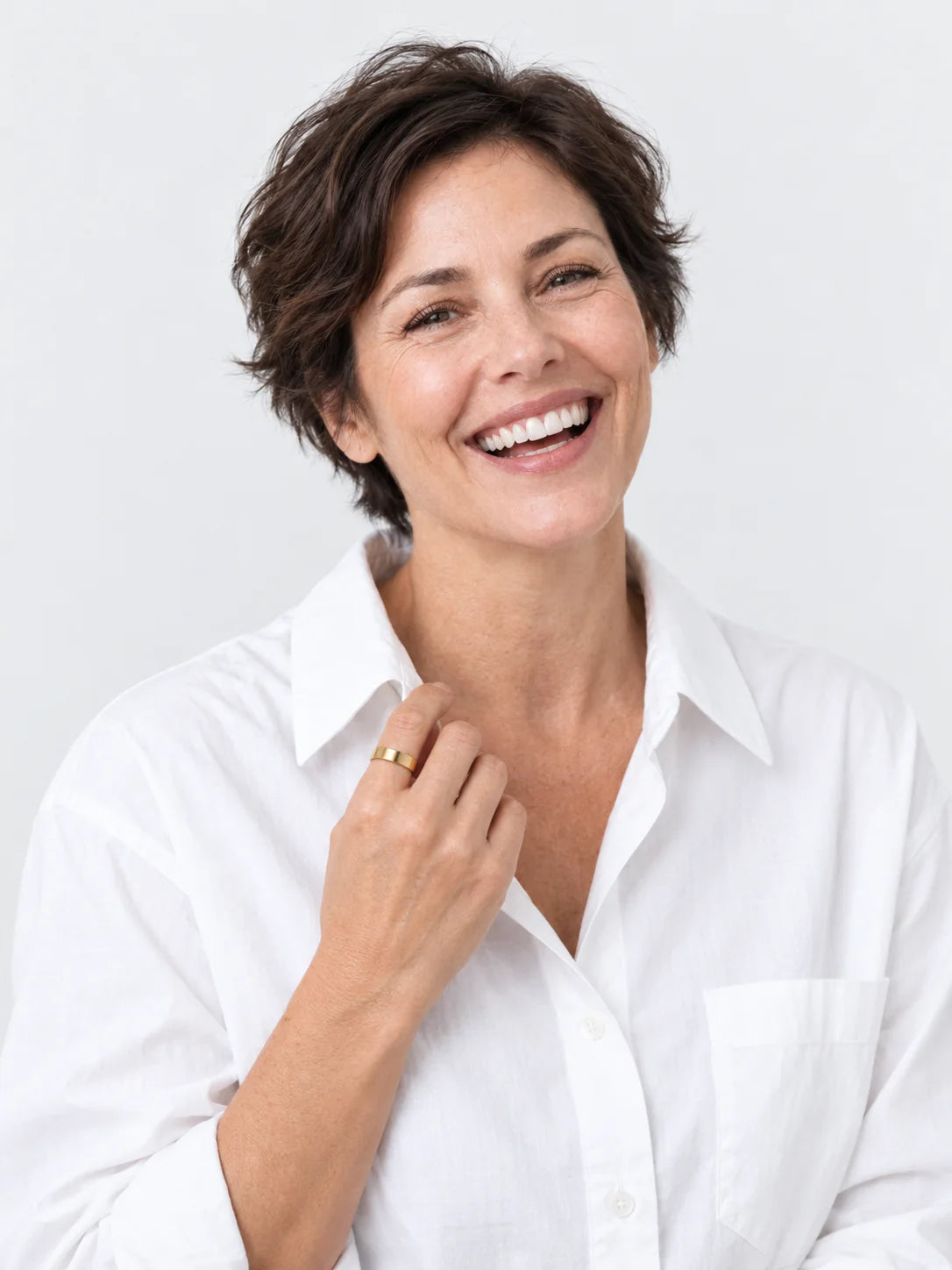 A woman in her late forties with short dark hair, laughing, the Vitality Ring on the hand at her collar