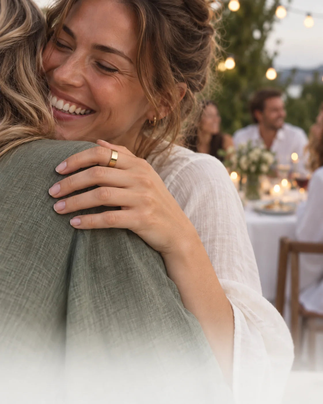 A woman hugs a friend hello at an evening birthday dinner, the Vitality Ring on her hand