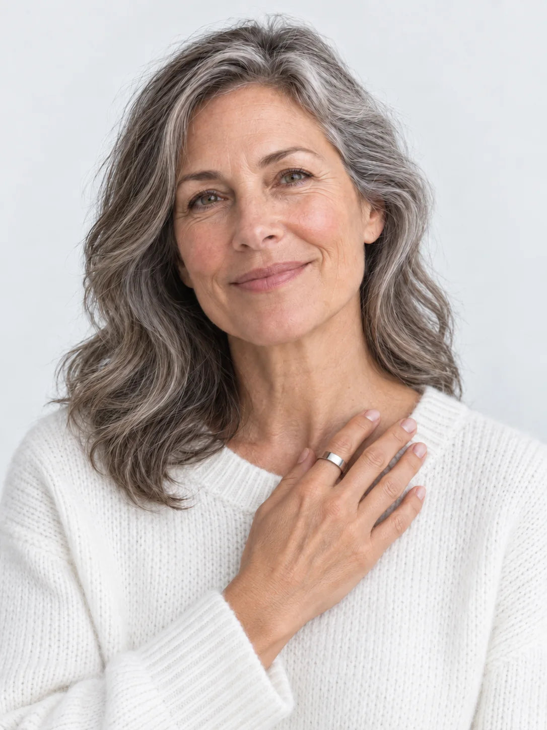 A woman in her fifties with silver-streaked hair, smiling, the Vitality Ring on the hand at her collarbone